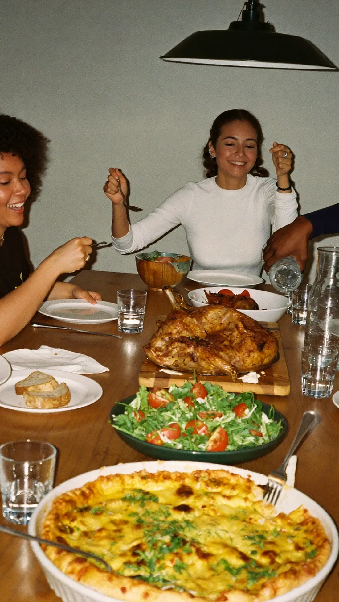 Six convives autour d’une grande table : un gratin doré, une salade, un poulet rôti et du pain partagés en riant.