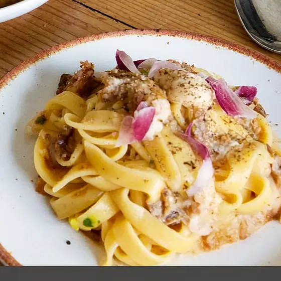 Un plat de tagliatelle à la crème, lardons et oignon rouge, dans une assiette blanche.