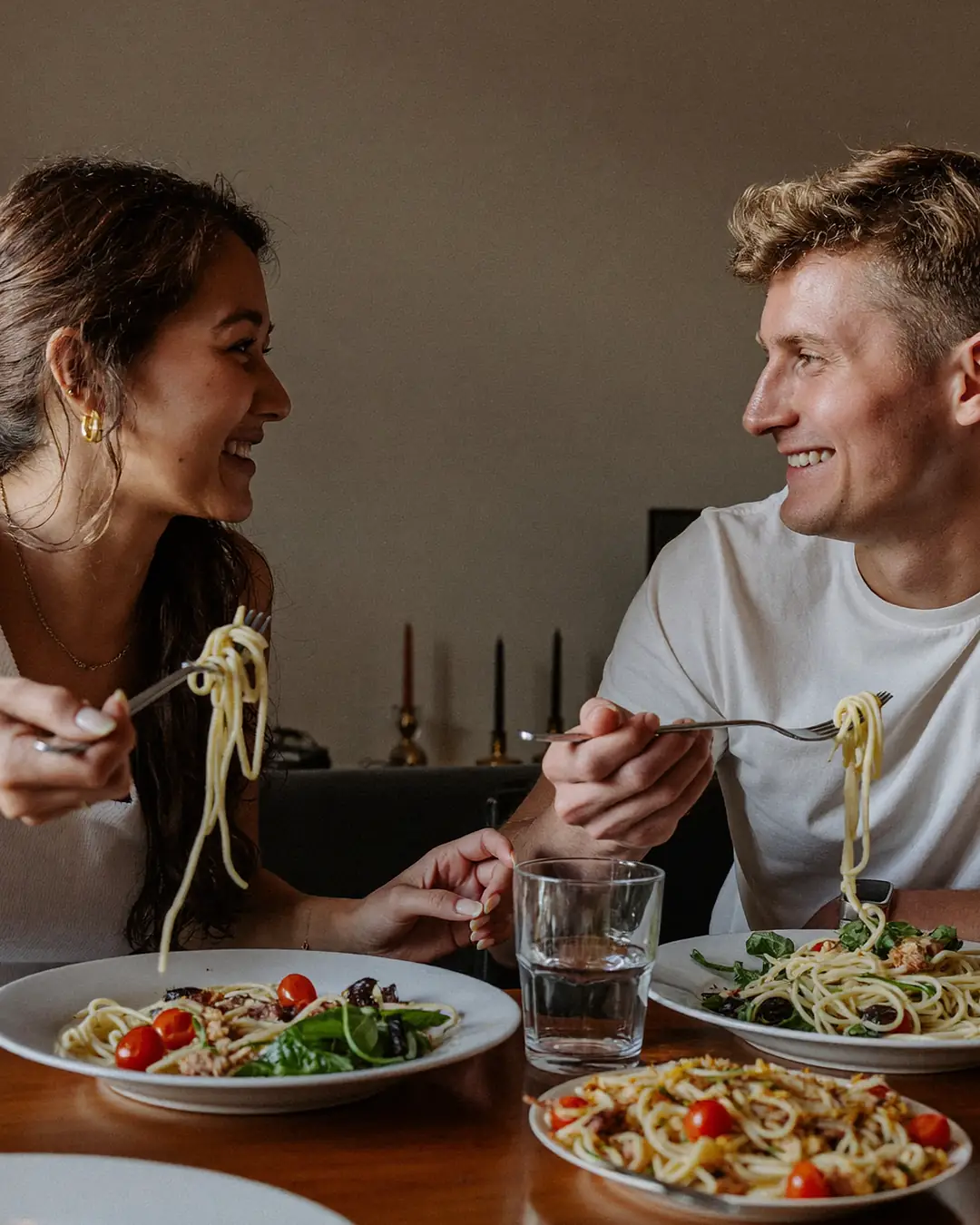 Un couple dîne à la maison un soir de semaine, en discutant autour d’un plat de pâtes.